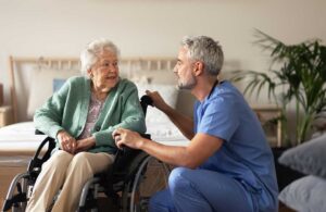 Adult child talking with an older relative at a kitchen table while reviewing medications and daily routines.